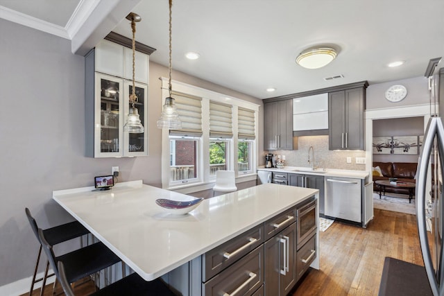 kitchen featuring stainless steel appliances, a sink, a breakfast bar area, light countertops, and glass insert cabinets