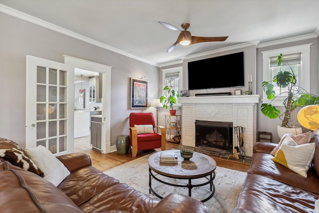 living room featuring ornamental molding, healthy amount of natural light, a brick fireplace, wood finished floors, and ceiling fan