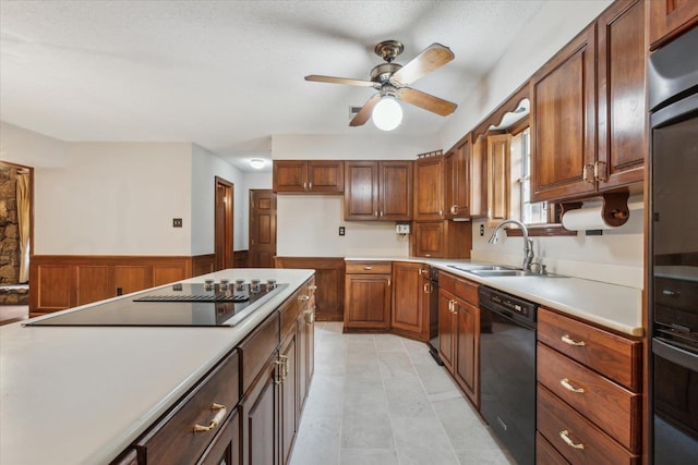 kitchen with black appliances, a sink, a wainscoted wall, a ceiling fan, and light countertops