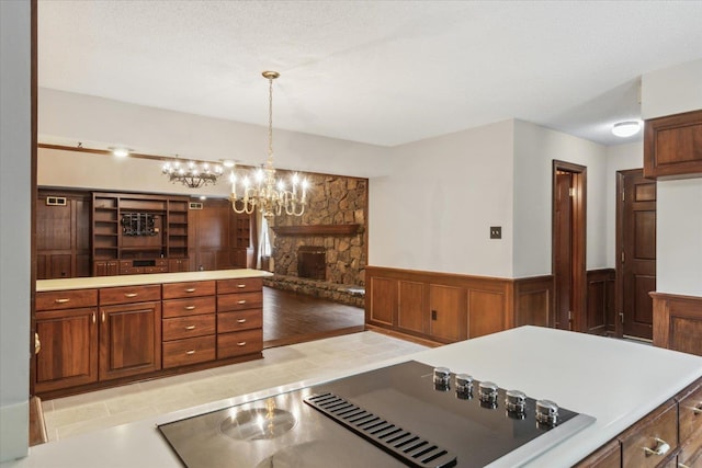 kitchen with black electric stovetop, wainscoting, a stone fireplace, a chandelier, and decorative light fixtures