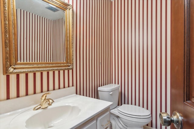 half bathroom featuring wallpapered walls, vanity, and toilet