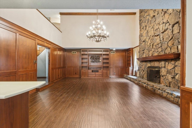 unfurnished living room with a towering ceiling, dark wood finished floors, a chandelier, and a fireplace