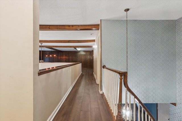 corridor with wood finished floors, an upstairs landing, beam ceiling, baseboards, and a textured ceiling