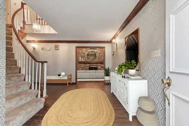 foyer featuring crown molding, dark wood-type flooring, stairway, wallpapered walls, and a stone fireplace