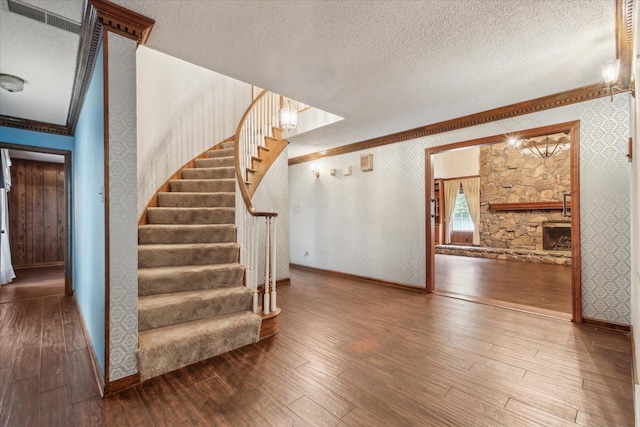 stairway with crown molding, hardwood / wood-style flooring, baseboards, a textured ceiling, and wallpapered walls