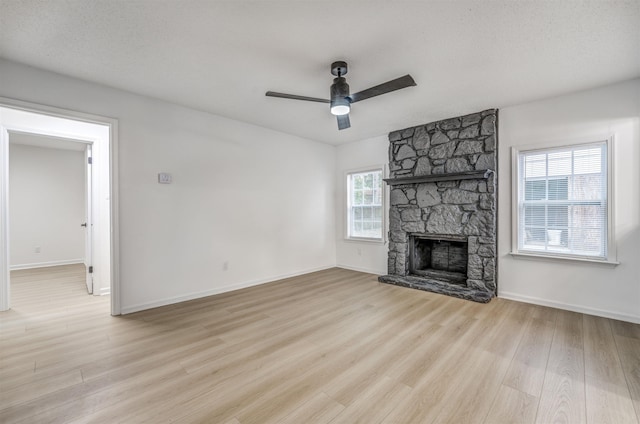 unfurnished living room featuring light wood-type flooring, a stone fireplace, baseboards, and a ceiling fan