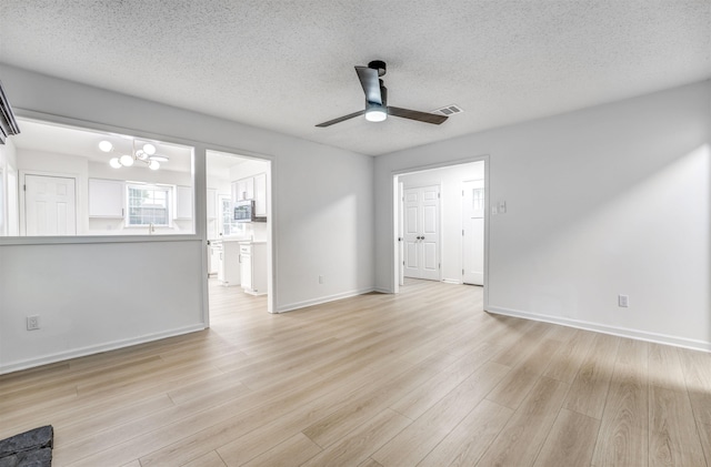 unfurnished living room with a ceiling fan, a textured ceiling, light wood-style flooring, baseboards, and a chandelier