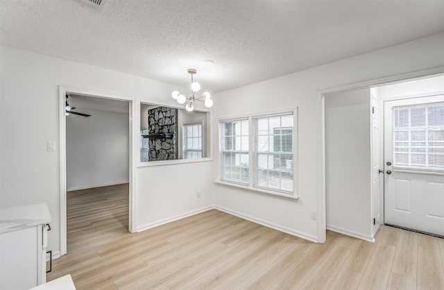 unfurnished dining area featuring a chandelier, light wood finished floors, a textured ceiling, and baseboards