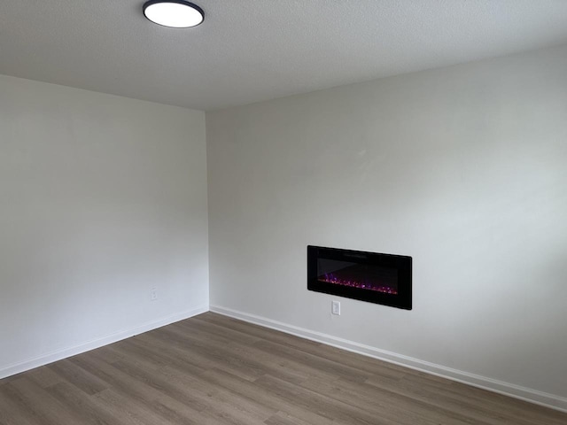 spare room featuring a glass covered fireplace, dark wood-style flooring, and baseboards