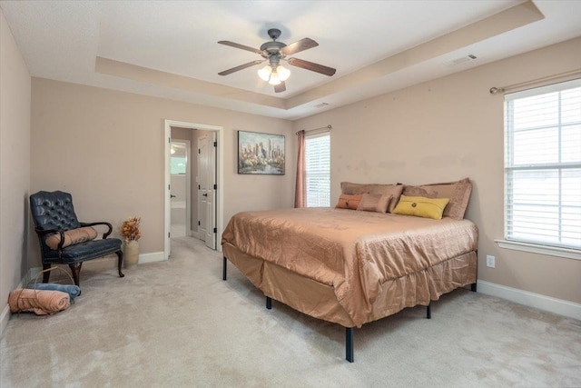 bedroom with a tray ceiling, light colored carpet, baseboards, and multiple windows