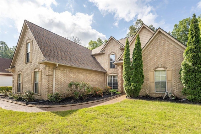 traditional-style home with brick siding, a front yard, and a shingled roof