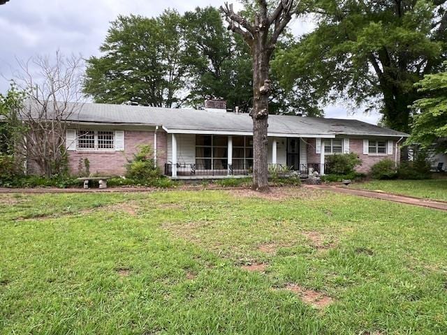 single story home featuring a front yard, brick siding, a porch, and a chimney