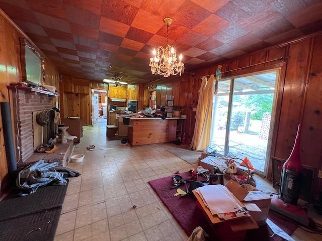living area featuring wood walls, a brick fireplace, a chandelier, light floors, and ceiling fan