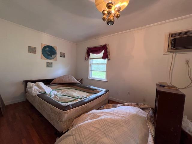 bedroom with an AC wall unit, ornamental molding, wood finished floors, and baseboards