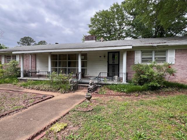 ranch-style home featuring covered porch, brick siding, and a chimney