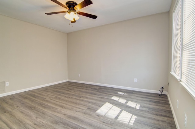 unfurnished room featuring healthy amount of natural light, a ceiling fan, wood finished floors, and baseboards