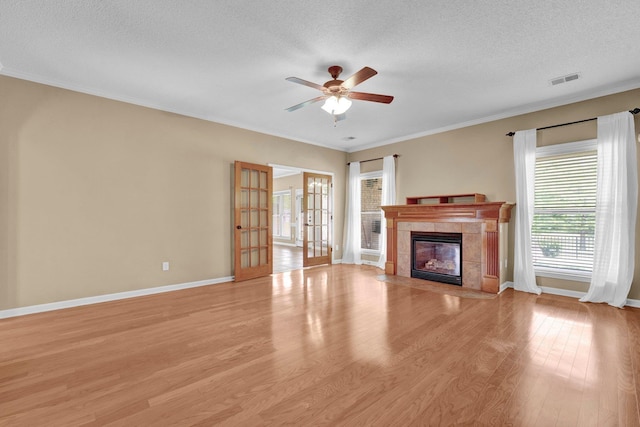 unfurnished living room with a tiled fireplace, light wood-style flooring, a ceiling fan, a textured ceiling, and french doors