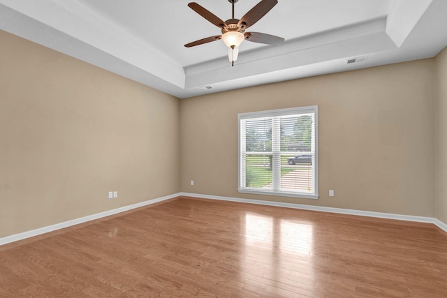 empty room with a tray ceiling, light wood finished floors, a ceiling fan, and baseboards