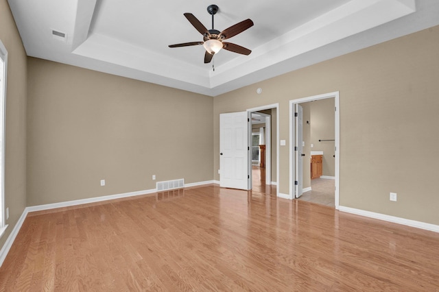 unfurnished bedroom featuring a raised ceiling, light wood-style flooring, and baseboards