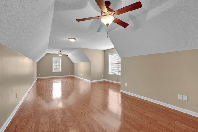 additional living space with a ceiling fan, a textured ceiling, plenty of natural light, vaulted ceiling, and light wood-type flooring