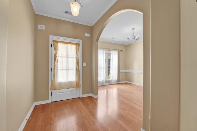 entrance foyer featuring arched walkways, wood finished floors, baseboards, ornamental molding, and a chandelier