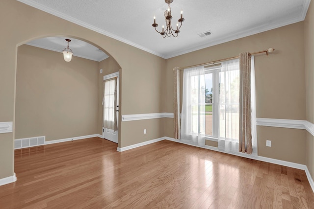 spare room with arched walkways, wood finished floors, a chandelier, baseboards, and crown molding