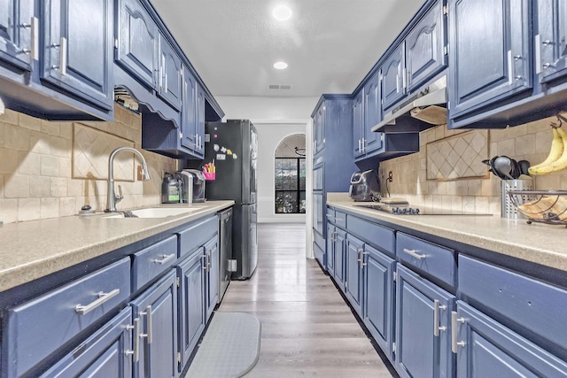 kitchen with a sink, blue cabinets, under cabinet range hood, stainless steel appliances, and recessed lighting