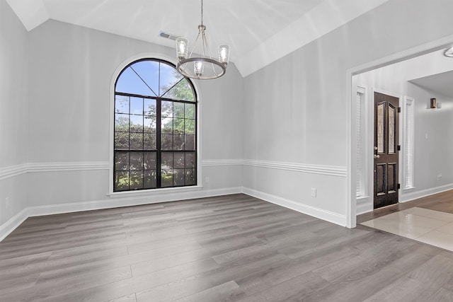 unfurnished dining area with vaulted ceiling, a chandelier, wood finished floors, and baseboards