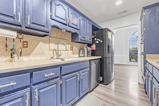 kitchen with stainless steel appliances, a sink, blue cabinets, and light wood-style flooring