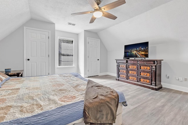 bedroom featuring vaulted ceiling, light wood-type flooring, a textured ceiling, baseboards, and ceiling fan