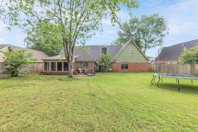 rear view of house featuring brick siding, a trampoline, and a sunroom