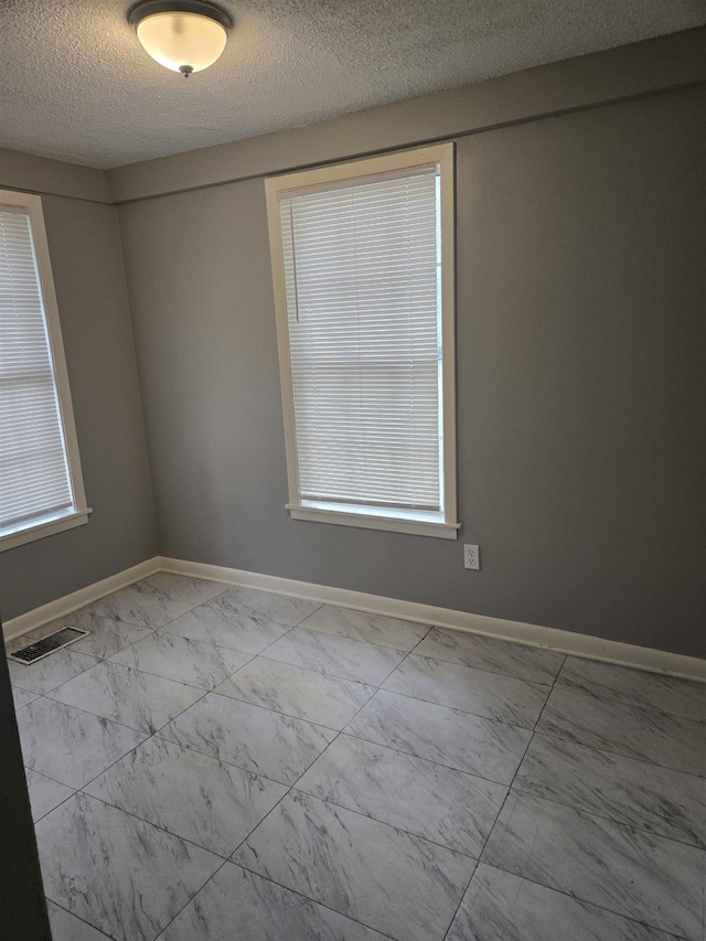 empty room with a textured ceiling, marble finish floors, and baseboards