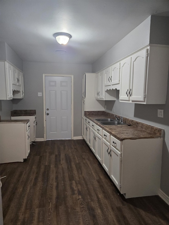 kitchen featuring a sink, dark wood-style flooring, baseboards, white cabinetry, and dark countertops