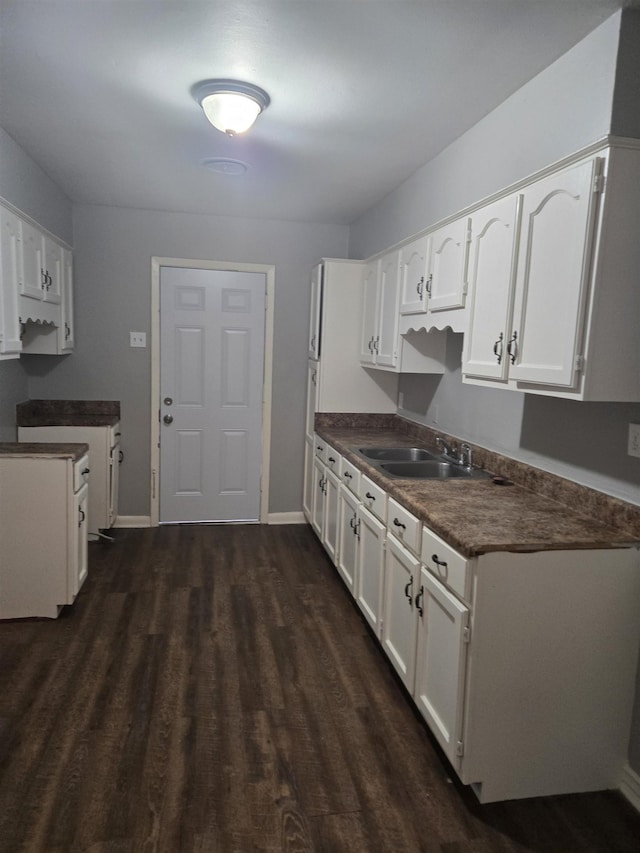 kitchen with a sink, dark countertops, dark wood-style floors, and white cabinetry