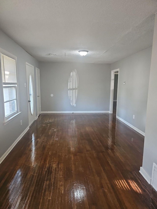 unfurnished living room with dark wood-style flooring, baseboards, and a textured ceiling
