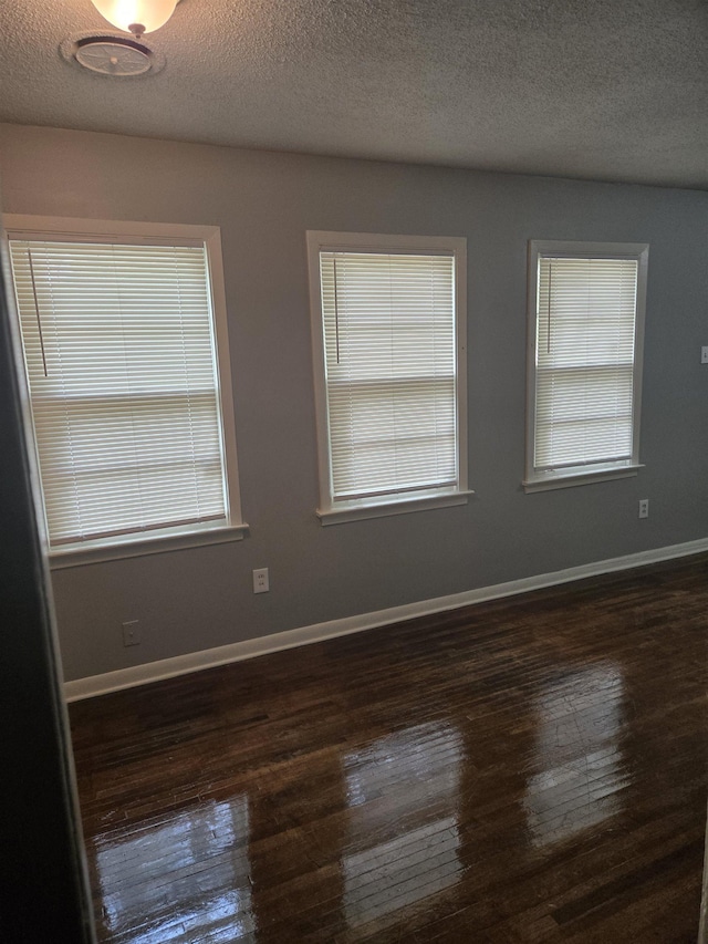 spare room with dark wood-style floors, a textured ceiling, and baseboards