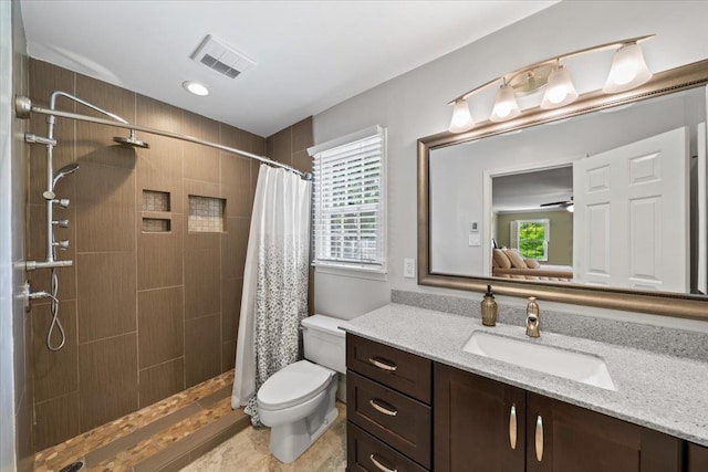 bathroom featuring toilet, a tile shower, vanity, and a ceiling fan