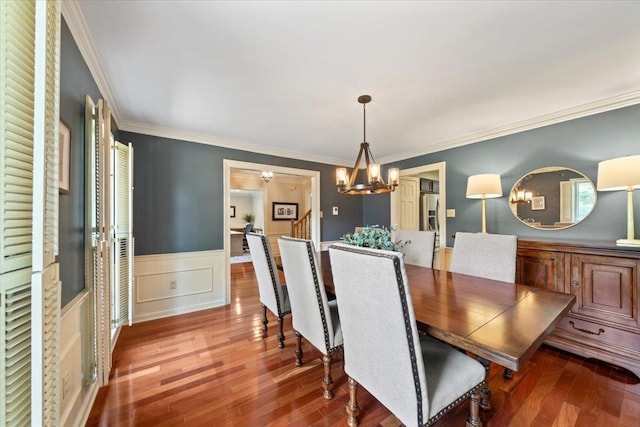 dining space with a chandelier, wood finished floors, a wainscoted wall, and crown molding