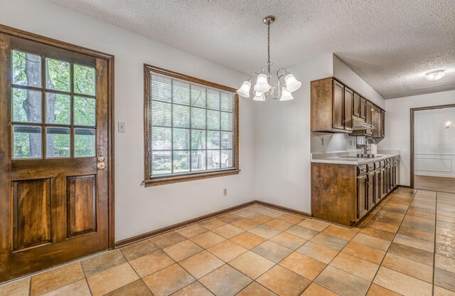 kitchen with a textured ceiling, a chandelier, light countertops, under cabinet range hood, and hanging light fixtures
