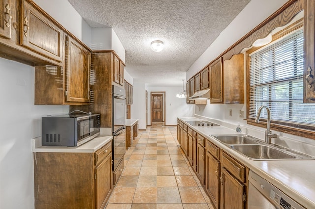 kitchen with black appliances, a sink, a textured ceiling, light countertops, and brown cabinetry