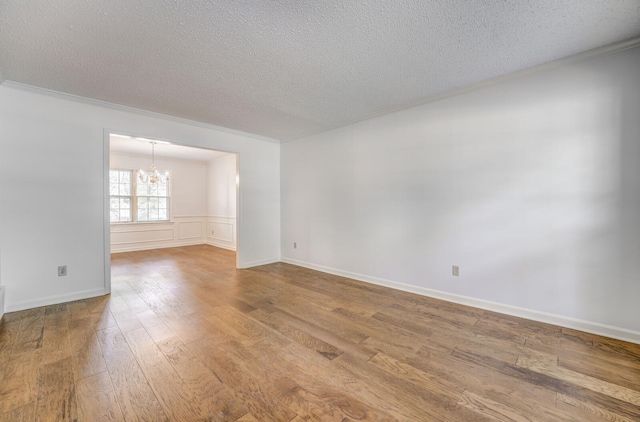 empty room featuring a chandelier, a textured ceiling, ornamental molding, and wood finished floors