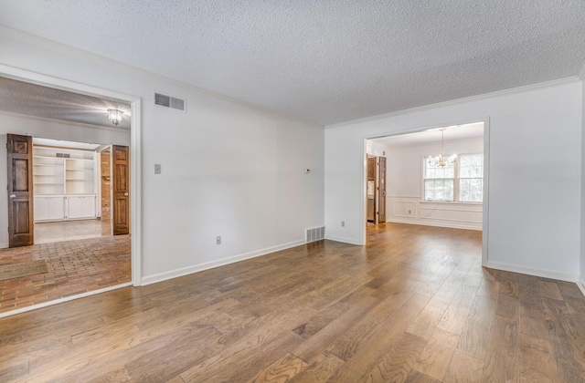 spare room with a chandelier, a textured ceiling, wood finished floors, and crown molding