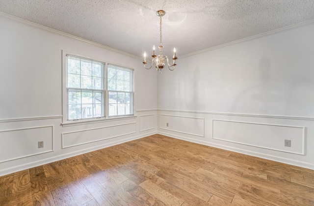 spare room featuring a chandelier, ornamental molding, light wood-type flooring, a textured ceiling, and wainscoting