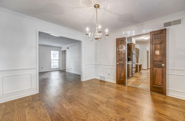 unfurnished dining area featuring a textured ceiling, ornamental molding, a chandelier, wood finished floors, and wainscoting