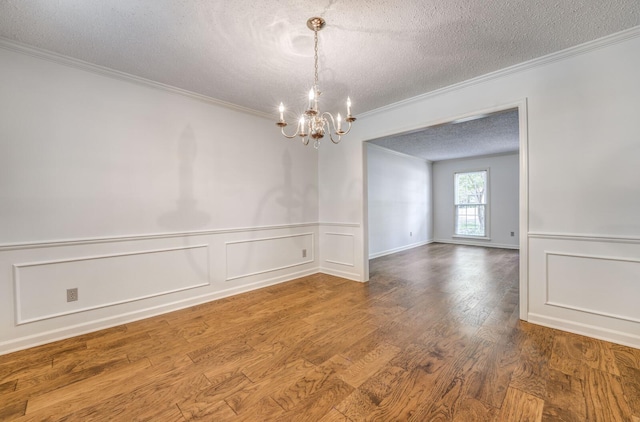 unfurnished room with a textured ceiling, ornamental molding, a chandelier, a decorative wall, and wood finished floors
