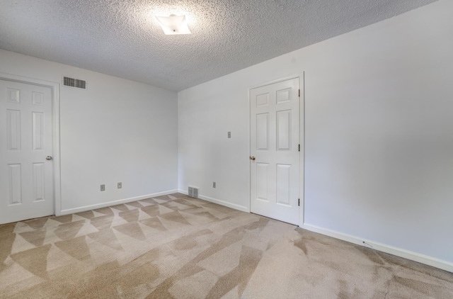 empty room with light colored carpet, a textured ceiling, and baseboards