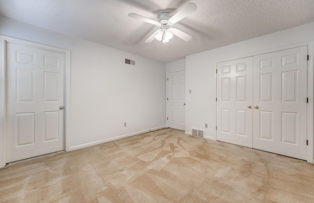 unfurnished bedroom featuring light colored carpet, a textured ceiling, baseboards, and ceiling fan