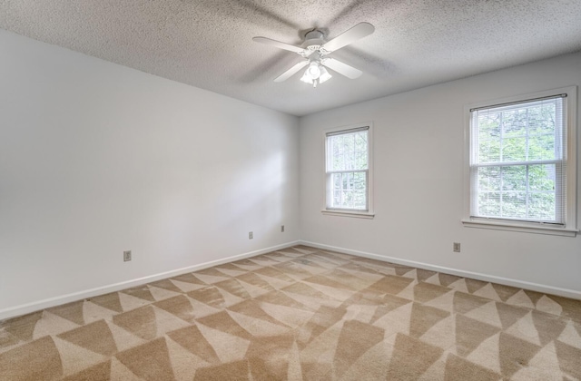 empty room with a textured ceiling, light colored carpet, ceiling fan, and baseboards