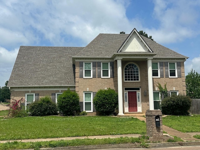 greek revival house featuring a front yard, brick siding, and roof with shingles