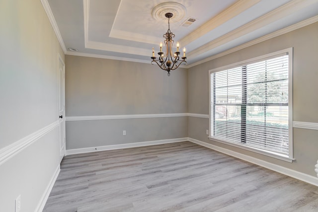 spare room with a chandelier, a raised ceiling, light wood-style floors, ornamental molding, and baseboards